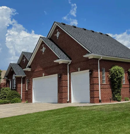 Red brick house with white garage doors and manicured lawn under blue sky