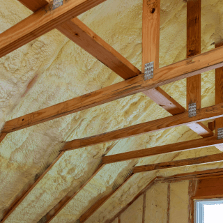 Yellow spray foam insulation installed between wooden roof rafters in attic