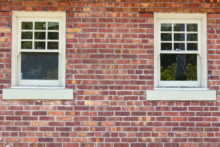 Two vintage windows on a red brick wall exterior of a building.
