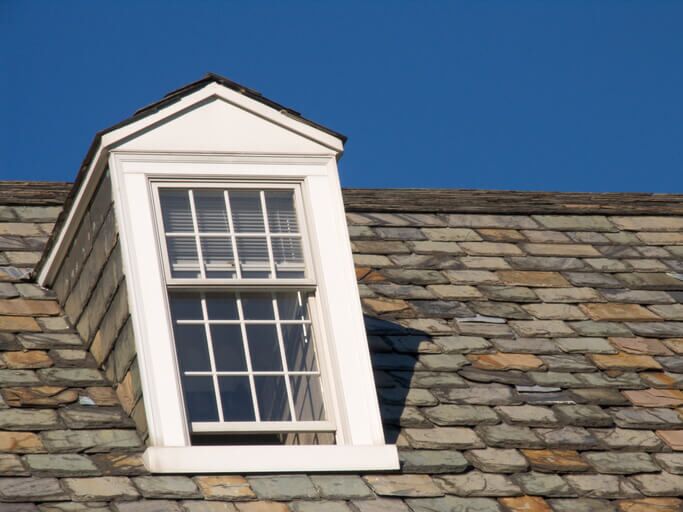 Dormer window on a slate roof against clear blue sky