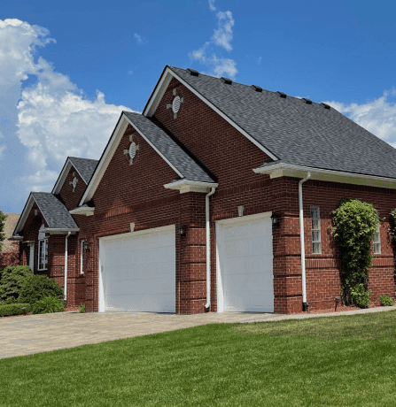 Red brick house with white garage doors and manicured lawn under blue sky