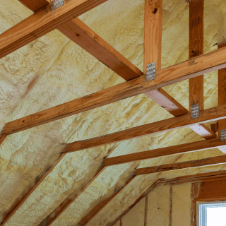 Yellow spray foam insulation installed between wooden roof rafters in attic