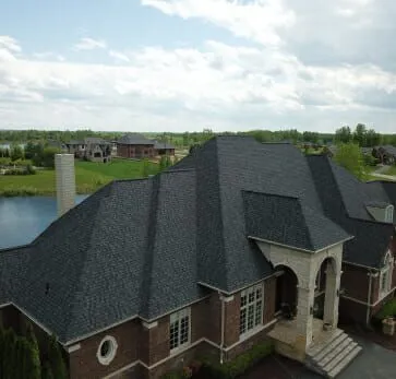 Aerial view of luxury brick home with dark shingle roof in waterfront community