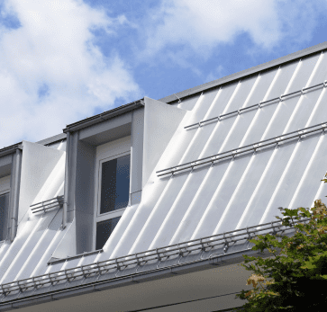 Modern white house with solar panels on metal roof against blue cloudy sky