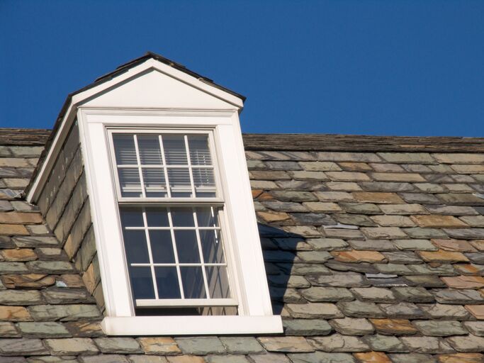 Dormer window on a slate roof against clear blue sky