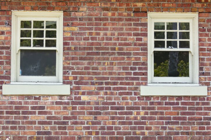 Two vintage windows on a red brick wall exterior of a building.