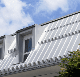 Modern white house with solar panels on metal roof against blue cloudy sky