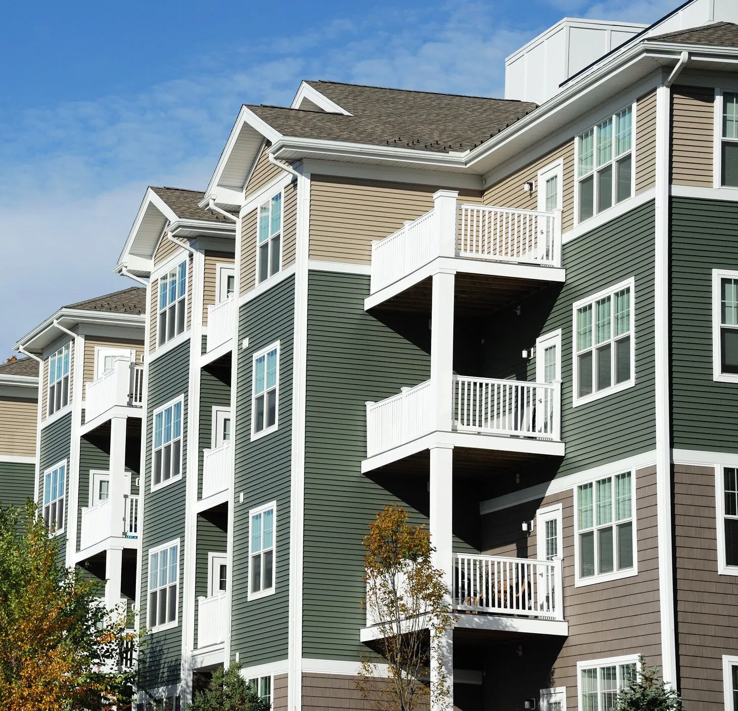 Modern apartment complex with green and tan siding featuring white balconies