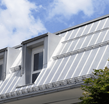 Modern white house with solar panels on metal roof against blue cloudy sky