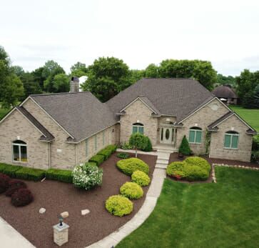 Aerial view of luxury stone house with curved driveway and landscaped yard