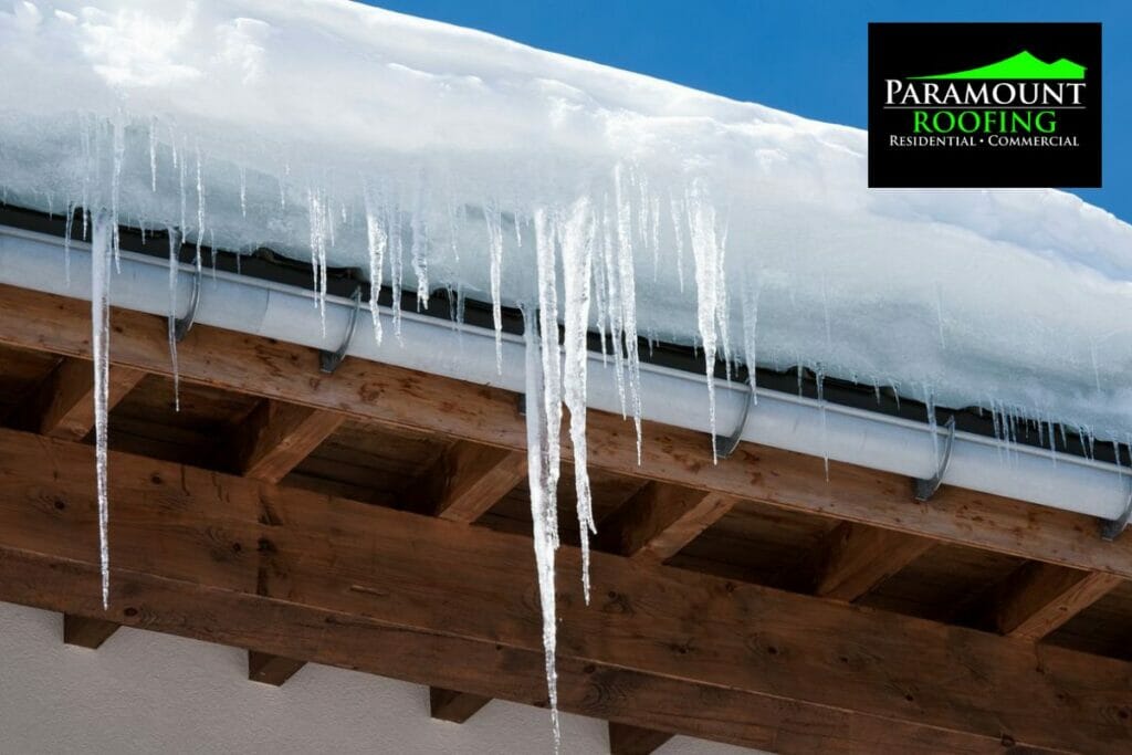 Heavy snow and icicles hanging from roof gutters showing winter roofing issues