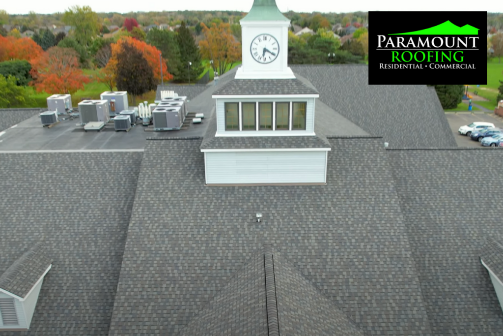 Aerial view of commercial building with gray shingle roof and clock tower in fall