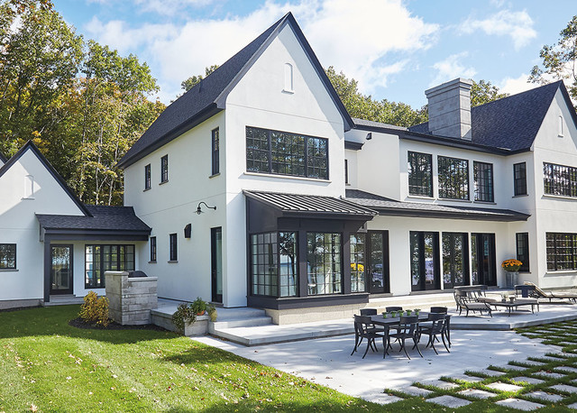 Modern white farmhouse with black trim and large windows surrounded by trees
