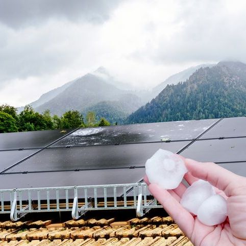 Hailstones held in hand above solar panels with a mountain backdrop.