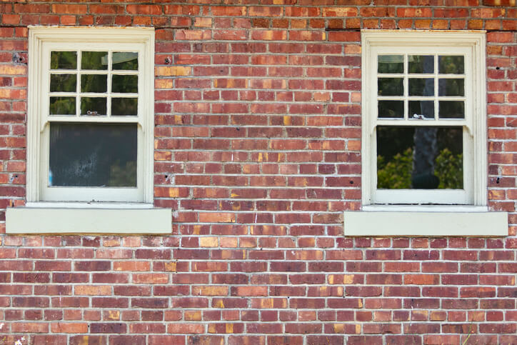 Two vintage windows on a red brick wall exterior of a building.
