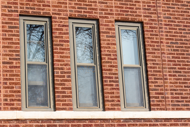 Three narrow windows on a red brick building wall.