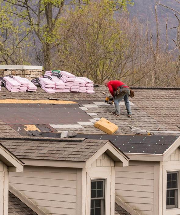 Roofer working on house roof with shingles and tools in springtime.