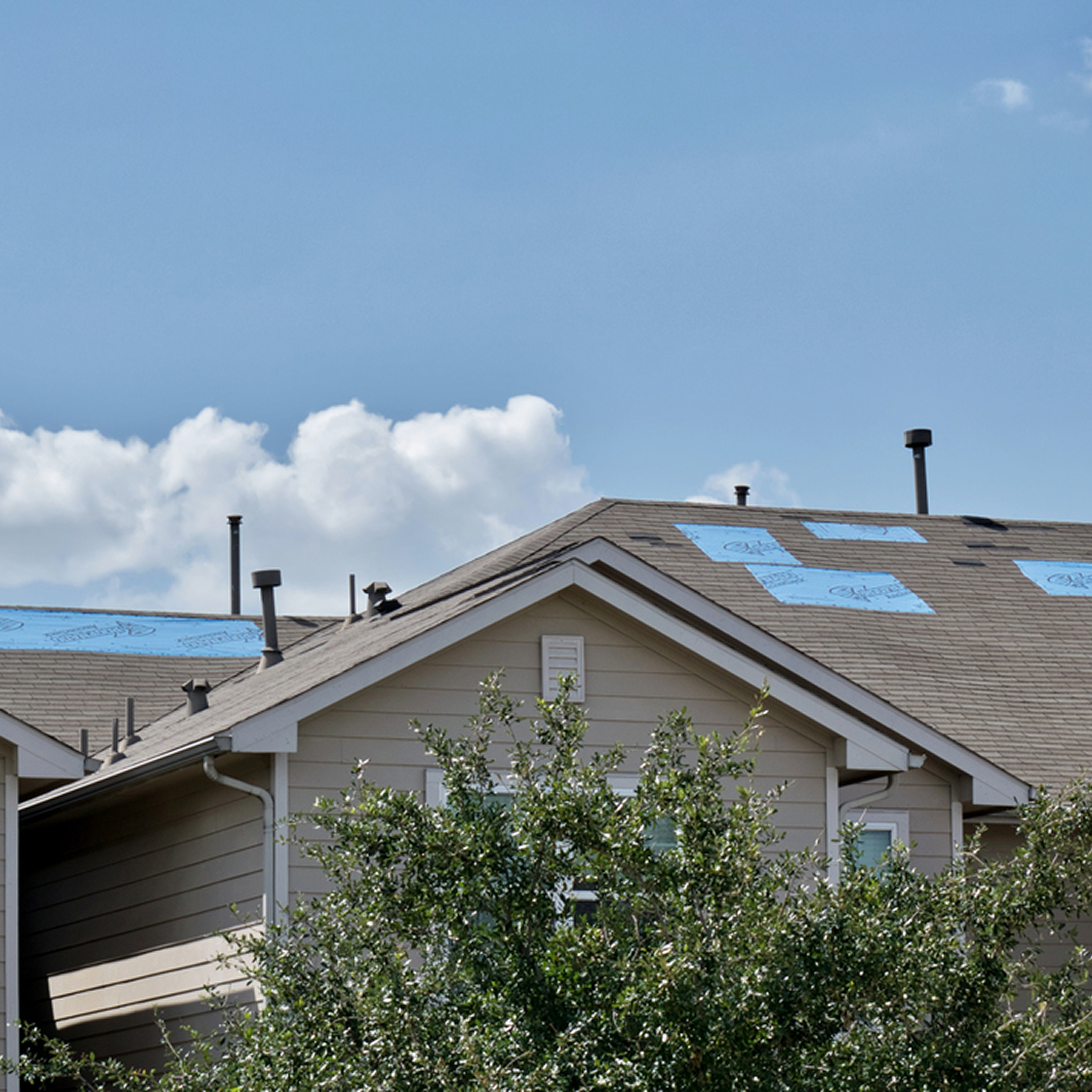 Residential home with roof under repair with blue tarp patches