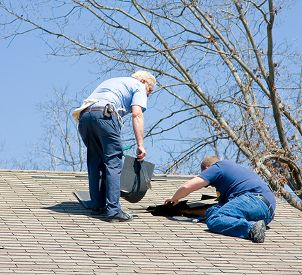 Two men working on roof repairs under clear blue sky