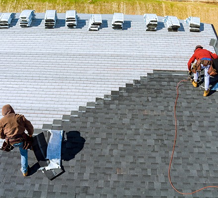 Roofers installing new shingles on a residential roof under a clear sky.
