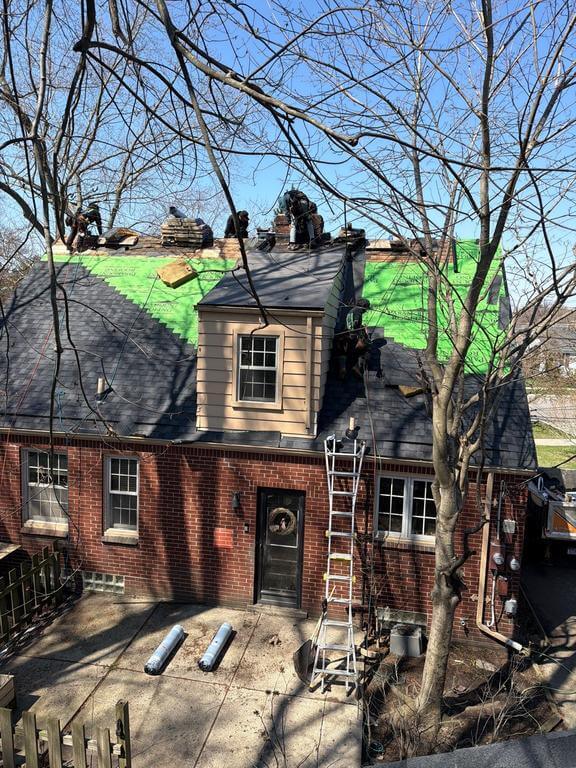 Workers repairing the roof of a brick house, using ladders and materials.
