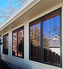 Modern house windows reflecting a clear blue sky and trees.