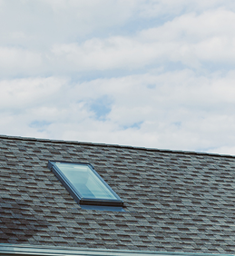 Skylight on a shingled roof under a partly cloudy sky.